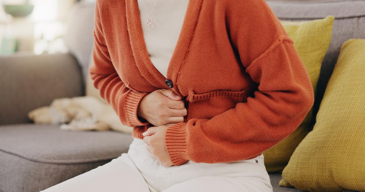 Person doubled over in pain suffering and holding belly on a couch.