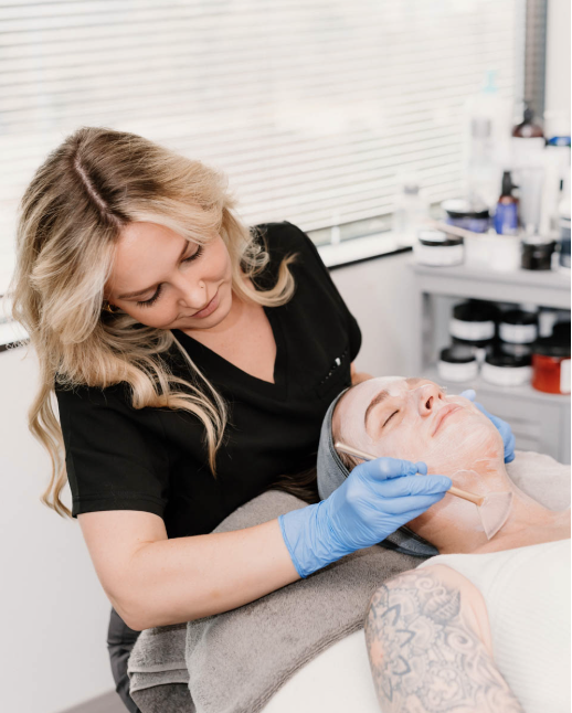 Skincare specialist wearing gloves applies a facial treatment to a relaxed client in our office.